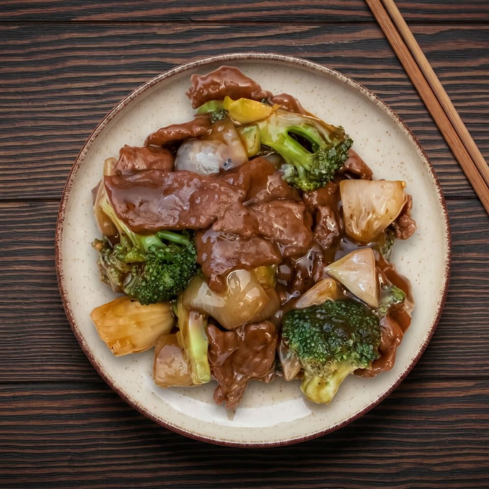 Beef and broccoli stir-fry with onions and peppers in a savory sauce, served on a plate with chopsticks.